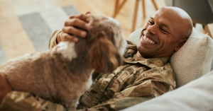 Lifestyle photo of man laughing and petting dog while lying on couch