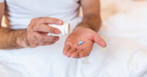 Man under covers pouring blue pill out of pill bottle into hand