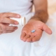 Man under covers pouring blue pill out of pill bottle into hand