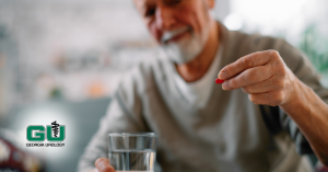 Man holding red pill in left hand and glass of water in right hand, smiling