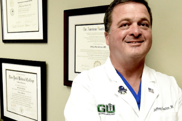 Urologist Dr. Jeffrey Proctor standing in front of his accolades in his office.