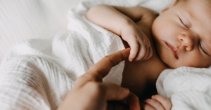 Newborn baby boy swaddled, holding father's finger