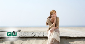 Woman looking off in distance sitting on wooden pier on sandy beach