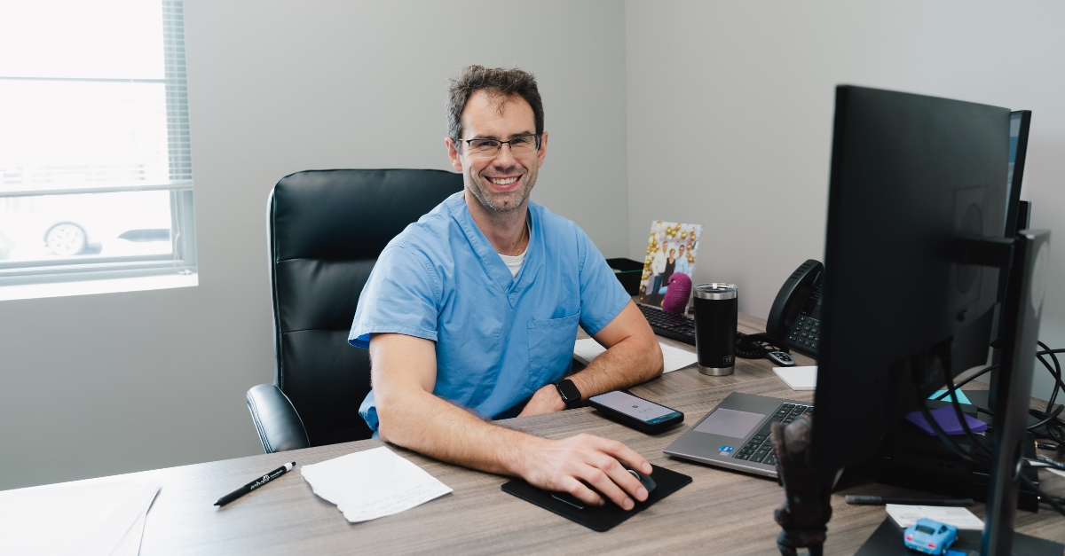 Dr. Dovirak sitting at desk in front of monitor screen smiling