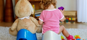 Child potty training next to stuffed bear