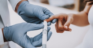 Doctor in blue gloves uses lancing device on diabetic patient