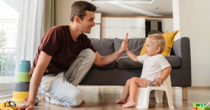 Dad and toddler son in living room, potty training child on mini toilet while hi-fiving fathe