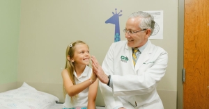 Dr. Andrew Kirsch sitting on patient chair with a little girl giving each other a highfive