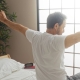 Man in bedroom sitting on bed stretching