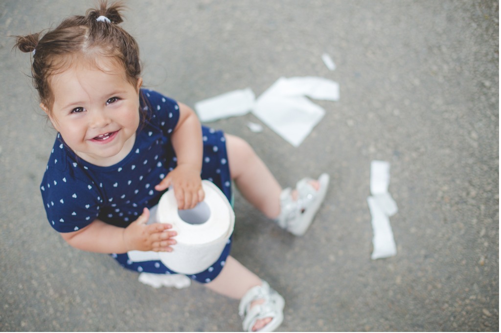 Little girl sitting outside with a toilet paper roll in her hand, working through potty training.