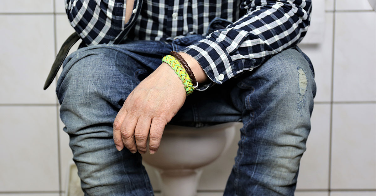 A young man sitting on a toilet struggling with bladder urgency and incontinence.