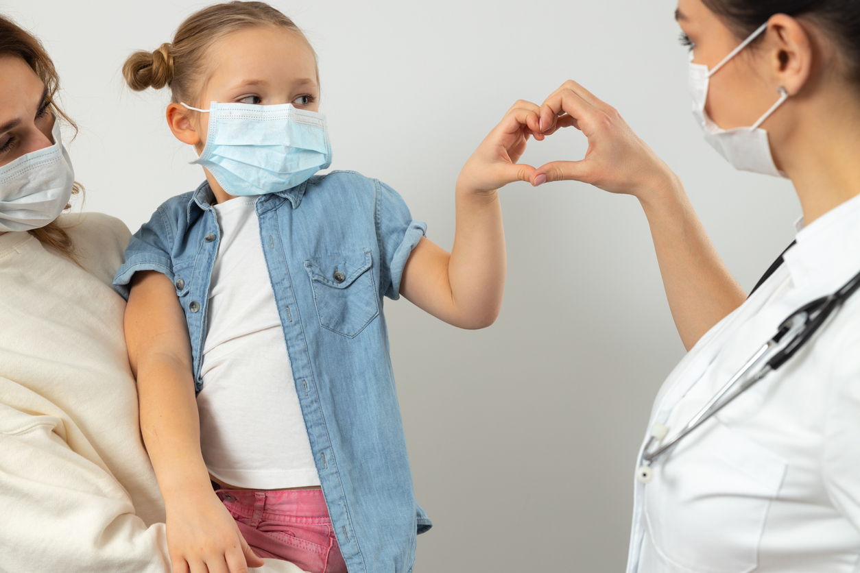 Female pediatrician making heart with hands with her little patient stock photo. Pediatrics concept