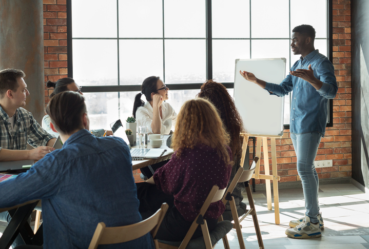 African-american team leader is lecturing his employees in loft office using white board, copy space.