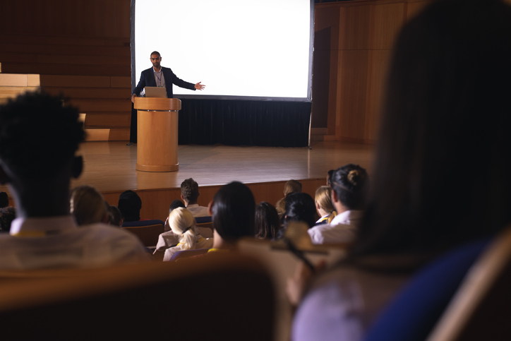 Front view of mixed race businessman giving presentation on white projector in front of the audience.