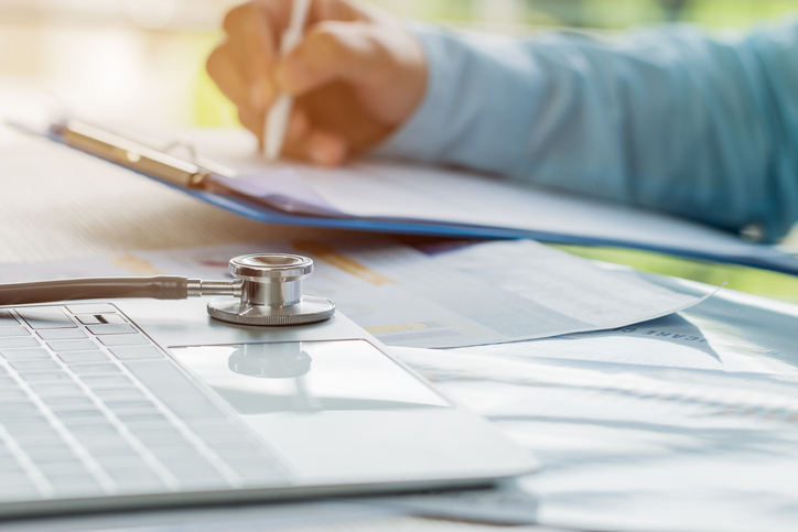 Doctor working in hospital writing prescription clipboard, working an Laptop on desk in hospital with report analysis, Healthcare and medical concept, selective focus.