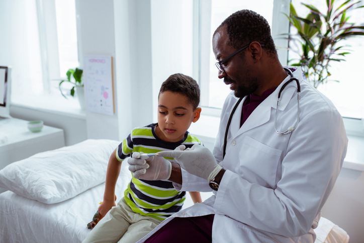 Showing boy thermometer. Pediatrician showing curious boy thermometer after measuring body temperature, the two discussing Nocturnal Enuresis.