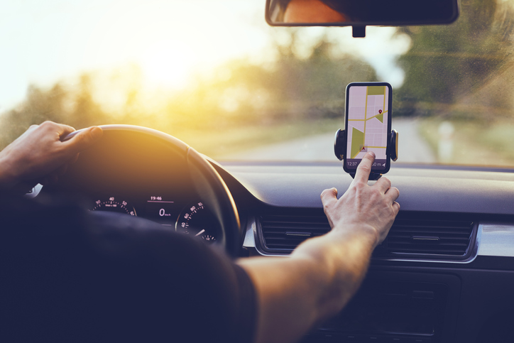 Driver using GPS navigation in mobile phone while driving car at sunset.