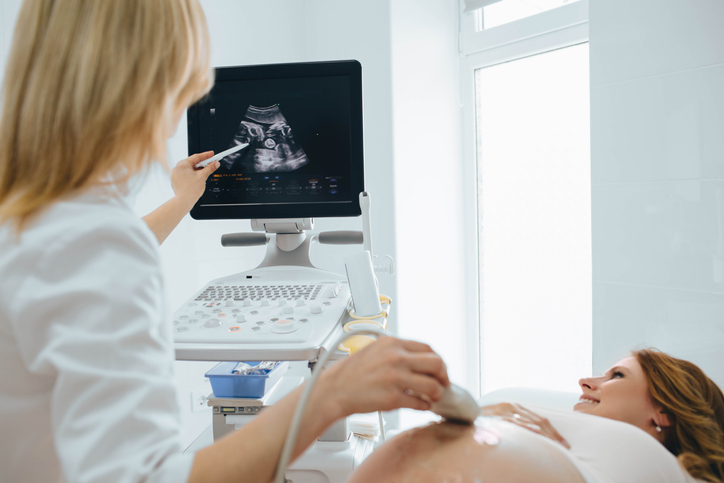 Happy woman looking at ultrasound results with her doctor in examination room, discussing Prenatal Hydronephrosis.