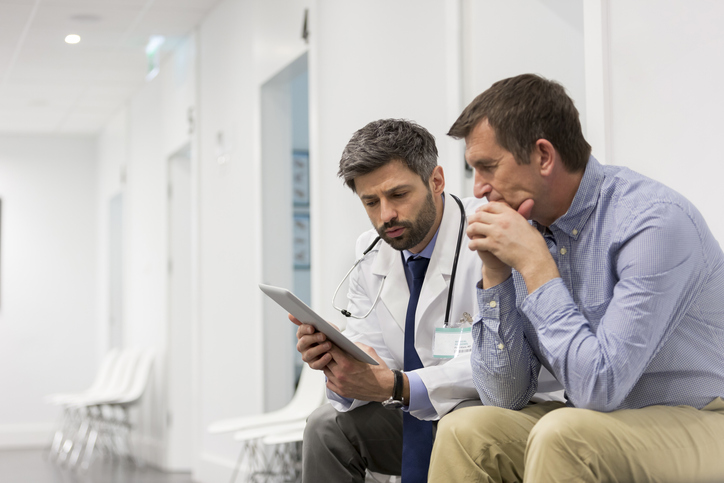 Mid adult doctor explaining serious patient over digital tablet at hospital.