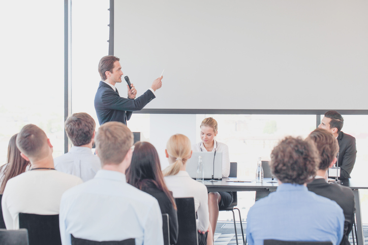 Speaker at business conference near white screen and audience.