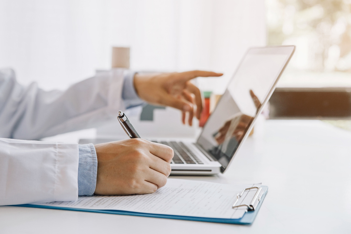 Doctor in hospital writing medical documentation and using laptop.