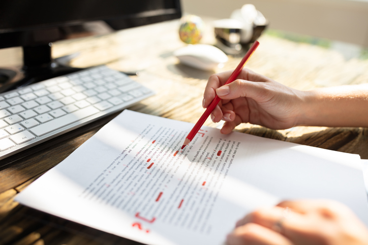 Close-up Of A Person's Hand Marking Error With Red Marker On Document.