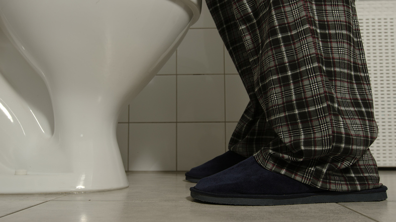 Closeup of male legs in a pajamas and slippers comes to a toilet, wondering Can Drinking Liquids at Night Increase Your Risk for Urologic Problems?