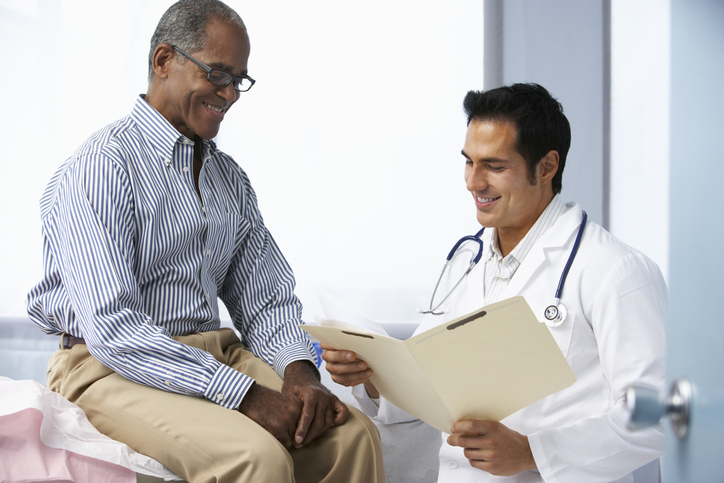 Doctor In Surgery With Male Patient Reading Notes Looking Happy, discussing the treatment options for erectile dysfunction.
