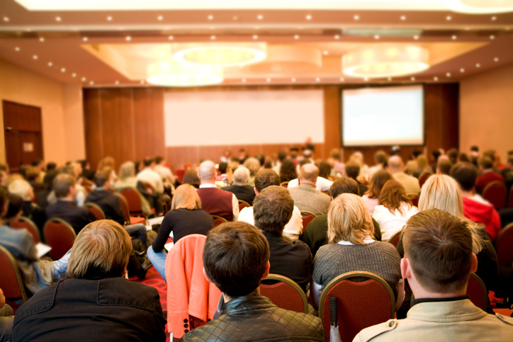 Rear view of many listeners sitting on chairs during lecture at conference.