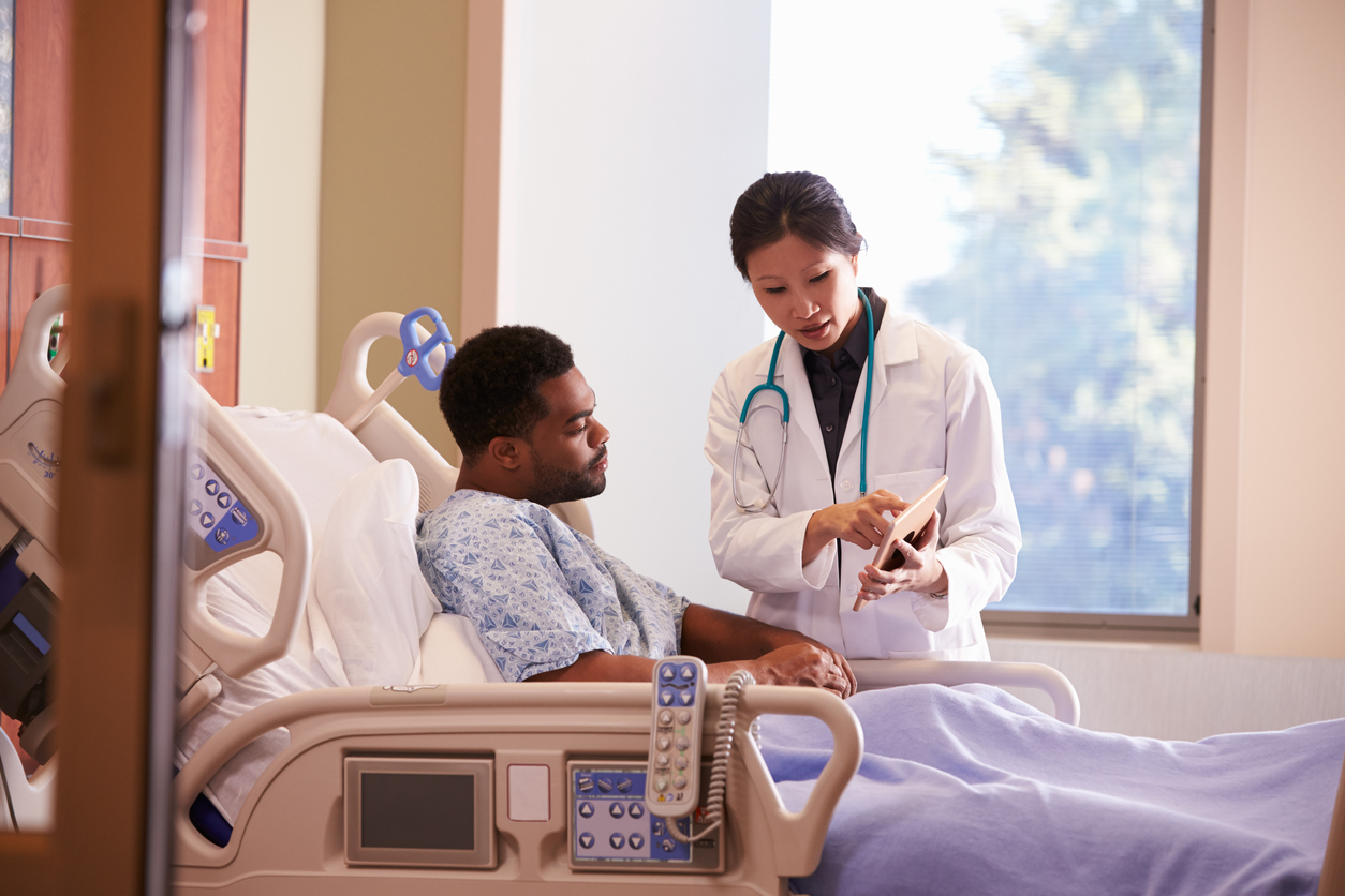 Hospital Doctor With Digital Tablet Talks To Male Patient, talking about PSA Rises After Surgery.