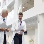 Two Doctors Talking As They Walk Through Modern Hospital, discussing benign Prostatic Hyperplasia