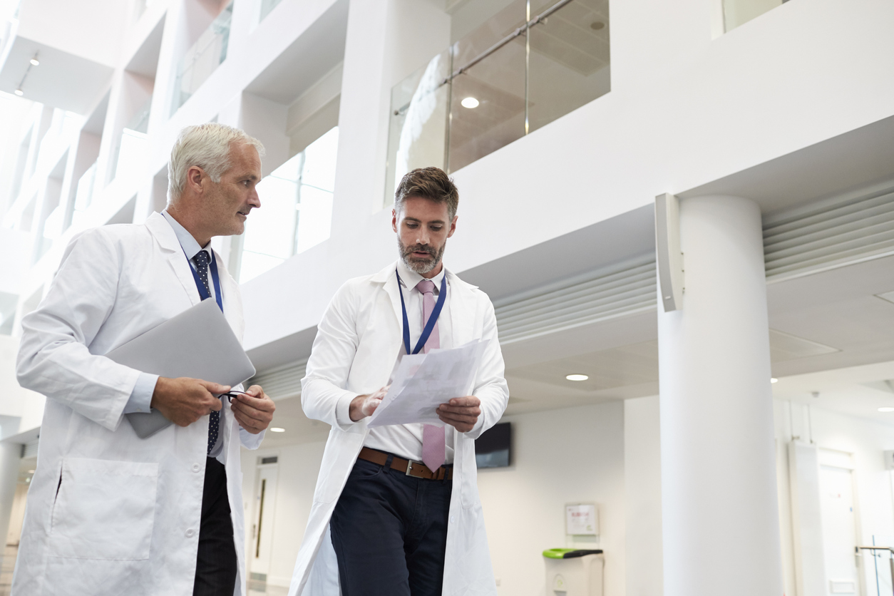 Two Doctors Talking As They Walk Through Modern Hospital, discussing benign Prostatic Hyperplasia