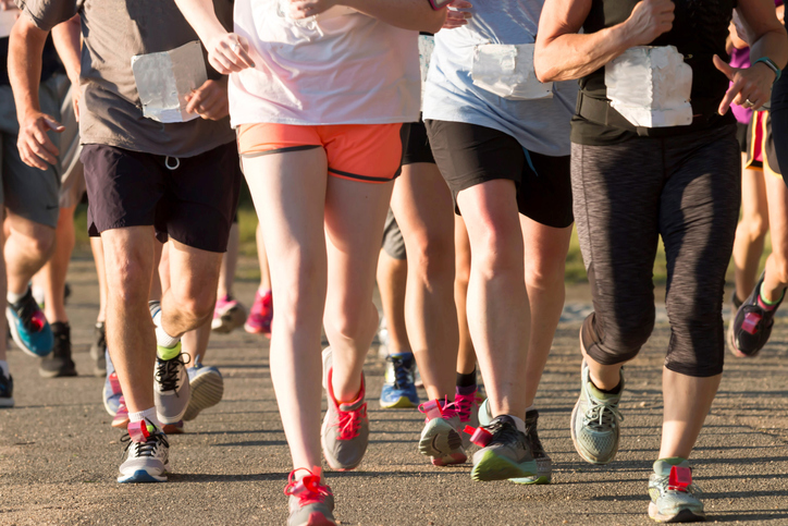 A pack of runners competiting in a local five thousand meter race, both men and women together, on a sunny summer early evening