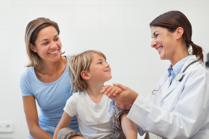 Smiling doctor auscultating the forearm of a child in examination room, discussing varicoceles in children.