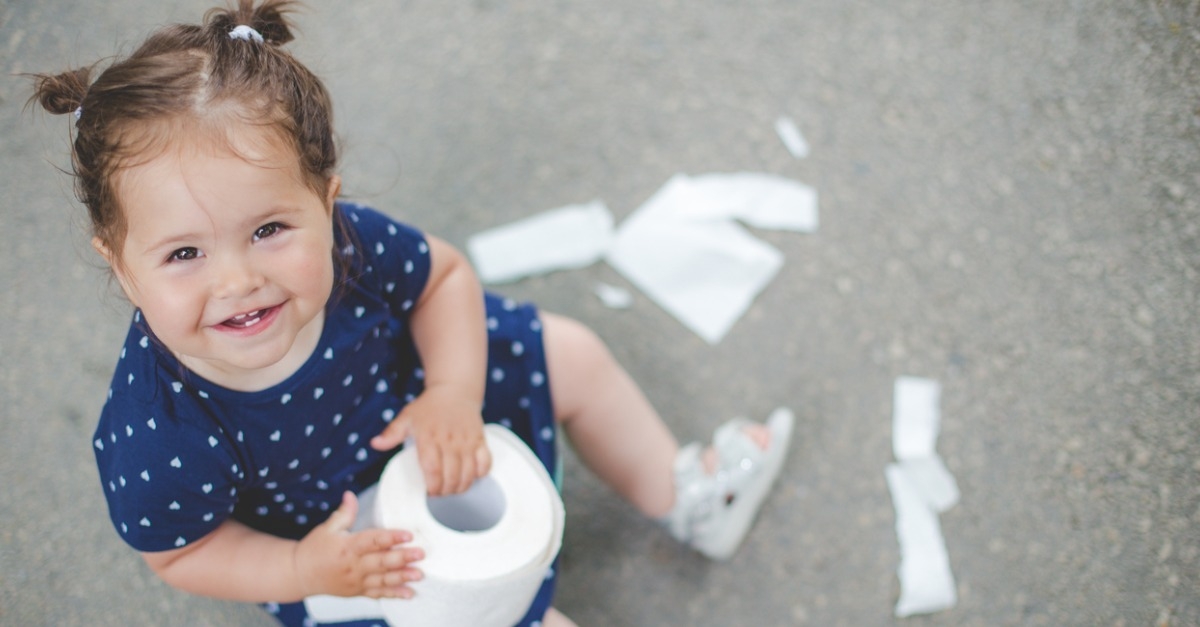 Little girl sitting outside with a toilet paper roll in her hand, working through potty training.