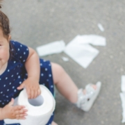 Little girl sitting outside with a toilet paper roll in her hand, working through potty training.