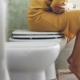 Woman sitting on toilet holding stomach